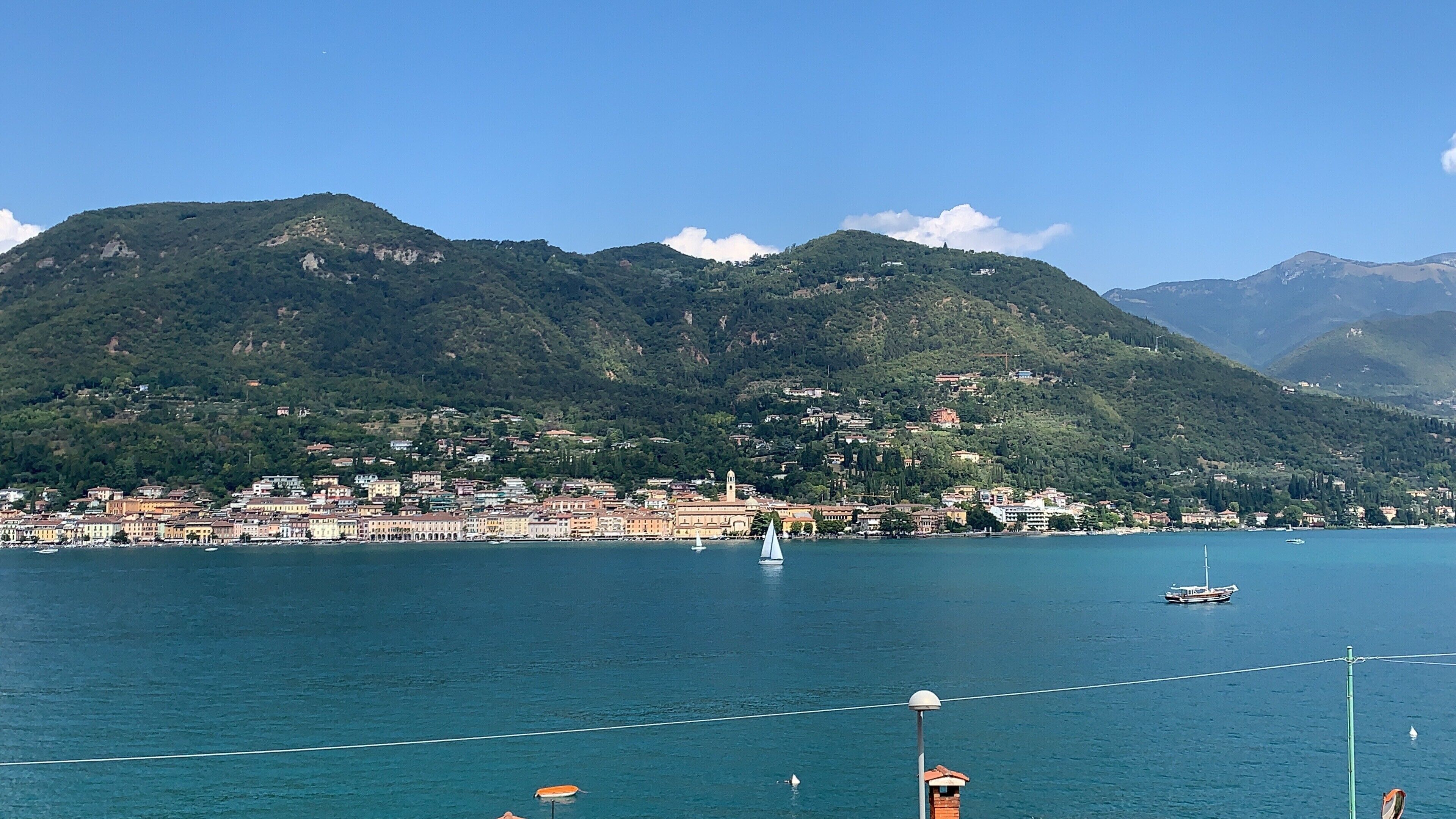 A coastal town with buildings along the waterfront, a sailboat, and mountains in the background.