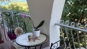 A small outdoor patio with a round table and a chair, surrounded by metal railings and potted plants.