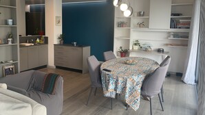 Una sala de estar moderna con una mesa de comedor, sofás grises y una zona de cocina con armarios y un fregadero.