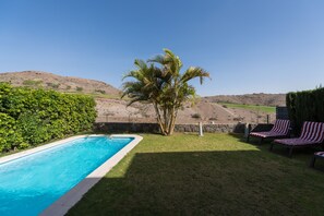 A swimming pool with a view of hills, a palm tree, and lounge chairs.