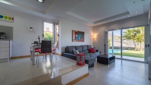 Ein modernes Wohnzimmer mit einer grauen Couch, einem Essbereich mit Tisch und Stühlen sowie einer großen Schiebeglastür zum Pool.