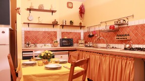 A kitchen with a dining table set for two, a microwave, a stove, and various kitchen utensils. - Naples 28 Holiday Home (Napoli)