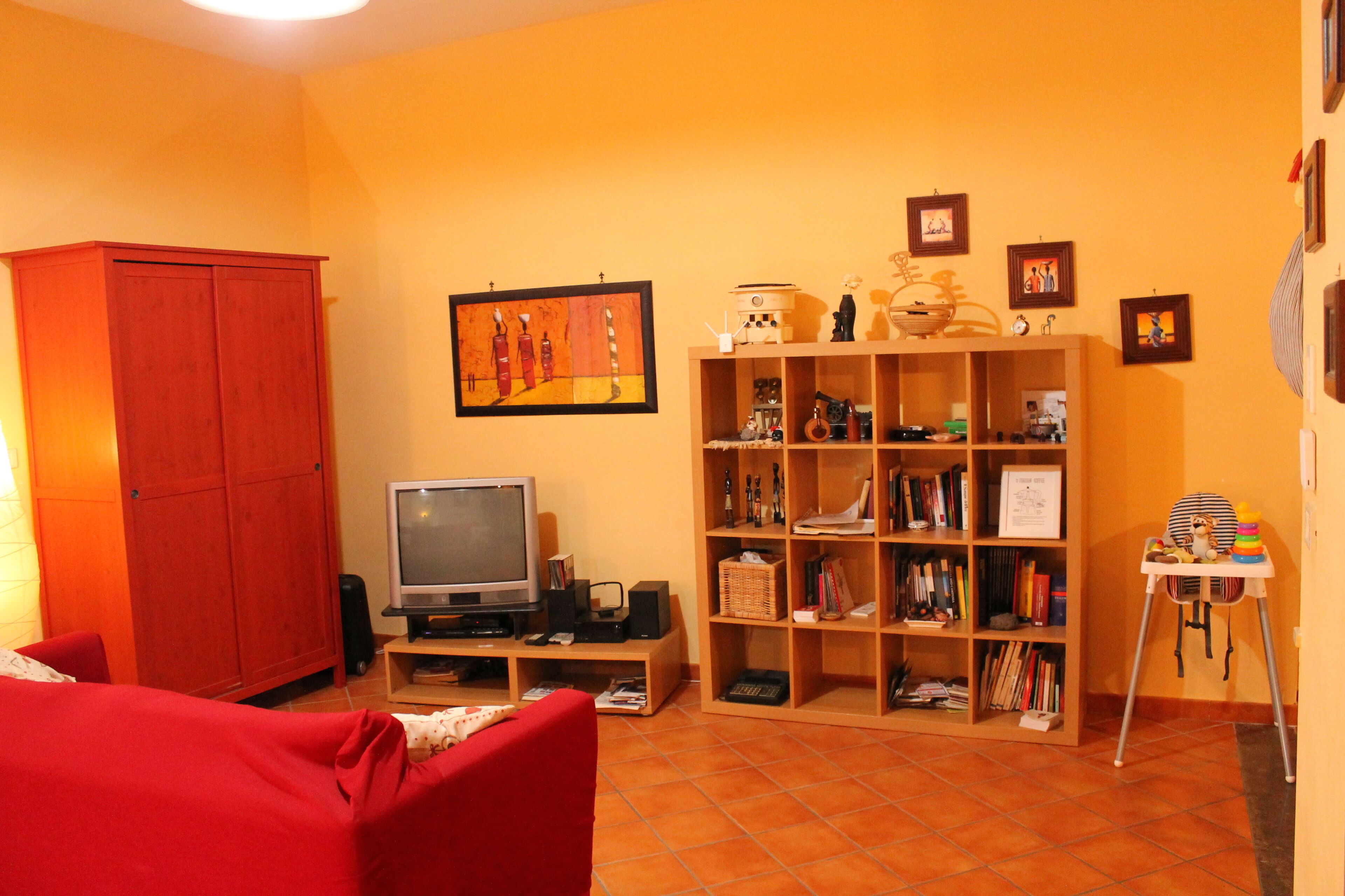 A living room with a red sofa, a television, a bookshelf, and a wooden cabinet.