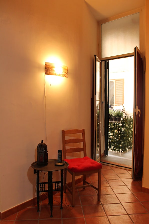 A corner room with a chair and a small table, a sliding glass door leading to a balcony, and a wall-mounted light fixture. - Vacation Home Naples 28 (Napoli)