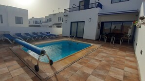En swimmingpool med blå liggestole, en vandrutsjebane og en flisebelagt terrasse.