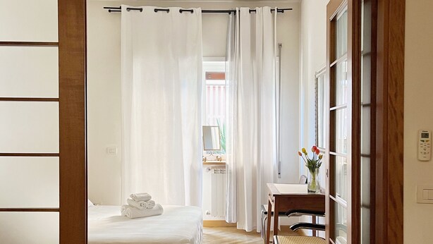 A hotel room with a bed, a desk with a chair, a window with curtains, and a wooden floor. - Relaxation in Rome away from the chaos - balcony, light and easy parking (Roma , Monte Sacro)