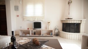 Ein Wohnzimmer mit Kamin, Fernseher auf einem Schrank und einem Tisch mit einer Weinflasche und Gläsern.