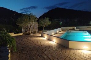 Una piscina amb un disseny modern, envoltada per un pati pavimentat amb una tanca decorativa i arbres.