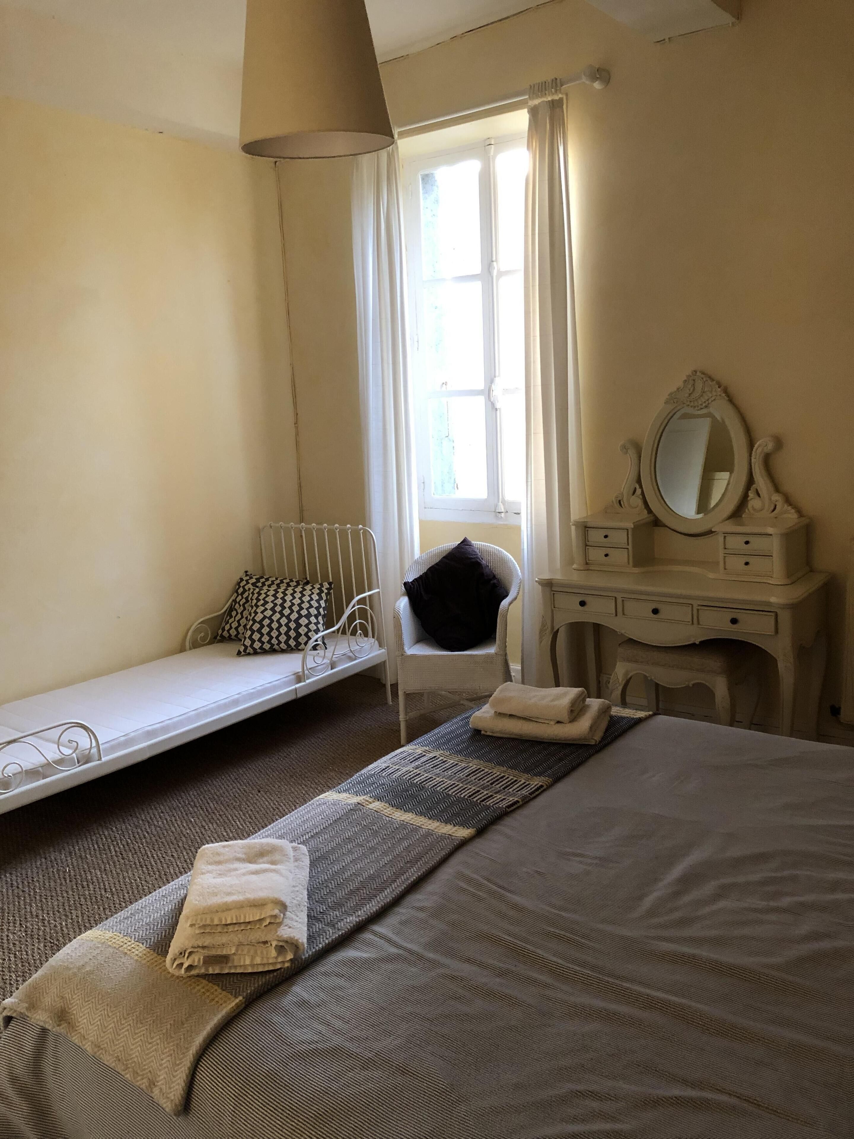 A bedroom with a bed, a chair, a dresser, and a window with curtains.