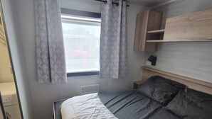 A bedroom with a bed, curtains, a window, a wooden shelf, and a small cabinet. - Mobile home 6 sleeps 4 * Domaine in the heart of the Loire Valley Castles  (Veuzain-Sur-Loire)