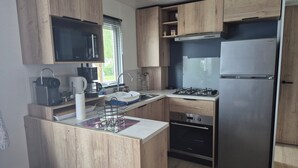 A compact kitchen with wooden cabinets, a built-in microwave, a gas stove, and a stainless steel refrigerator. - Mobile home 6 sleeps 4 * Domaine in the heart of the Loire Valley Castles  (Veuzain-Sur-Loire)