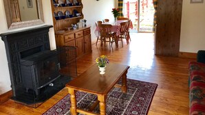 A cozy living room with a fireplace, wooden furniture, a dining area, and a view of the outdoors.