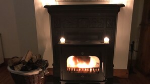 A fireplace with a lit fire, a basket of firewood, and a candle on the floor.