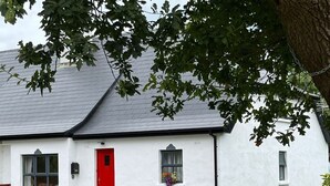 A white house with a red door, a grey roof, and a wooden fence in front.