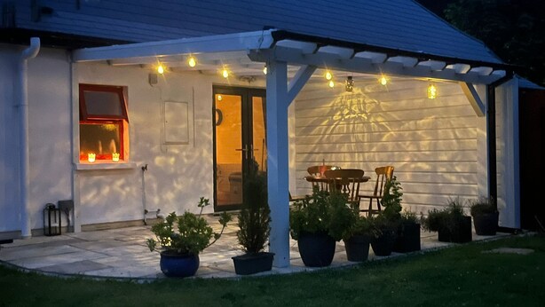 A covered patio area with a table and chairs, potted plants, and string lights.