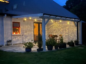 A covered patio area with a table and chairs, potted plants, and string lights. - #Charming Killarney Cottage (Aghadoe)