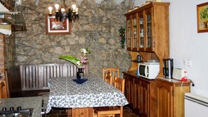 A cozy dining area with a stone wall, wooden furniture, a chandelier, and a cabinet with glass doors. - Oruna De Pielagos: Country Cottage / Gite - Santander (Oruña de Piélagos)