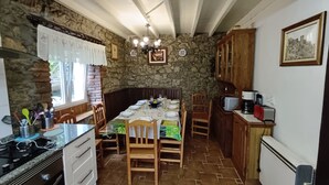 A cozy kitchen with a stone wall, wooden cabinets, and a dining table set for four. - Oruna De Pielagos: Country Cottage / Gite - Santander (Oruña de Piélagos)