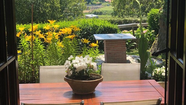 An outdoor dining area with a table and chairs, surrounded by lush greenery and flowers. - Oruna De Pielagos: Country Cottage / Gite - Santander (Oruña de Piélagos)
