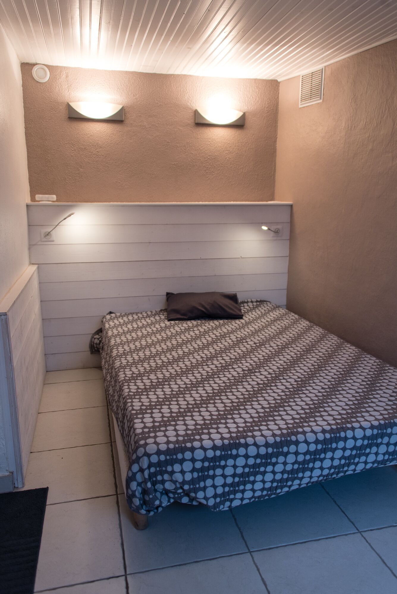 Een kleine, verzorgde slaapkamer met een bed, een kussen en twee wandlampen.