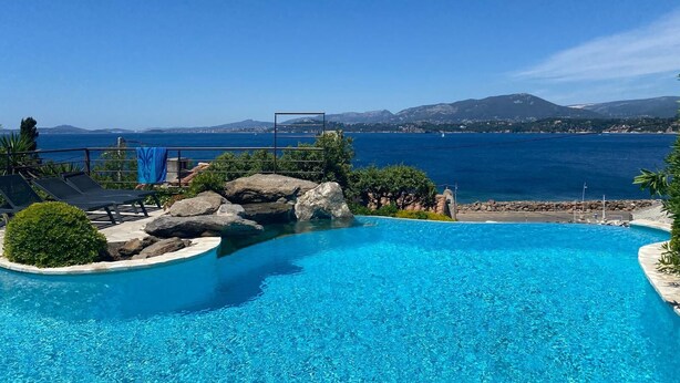 Una piscina de blau clar amb vistes al mar i a les muntanyes de fons.