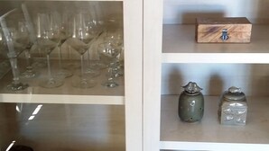 Um armário com vários compartimentos, incluindo um expositor de vidro para copos de vinho, prateleiras com objetos decorativos e gavetas para armazenamento.