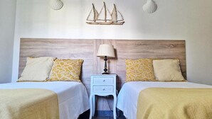 Quarto de hotel com duas camas, mesa de cabeceira com abajur e conchas decorativas na parede.