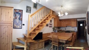 A kitchen with wooden cabinets, a wooden staircase, and a dining area with chairs and a table.