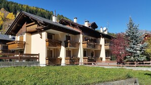 A multi-story chalet with wooden balconies, a stone facade, and a view of a forested hillside.