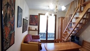 A cozy living room with a sofa, a wooden dining table, and a staircase.