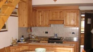 A wooden kitchen with a central island, a dining table with chairs, and a staircase leading to another level.