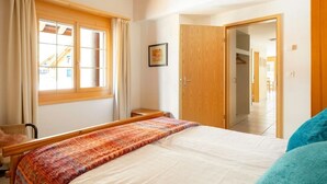 A bedroom with a bed, a window with curtains, a wooden door, and a hallway leading to another room. - Beautiful apartment with balcony and waterfall view (Lauterbrunnen)