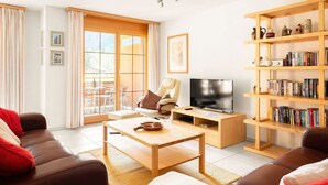 A modern living room with a sofa, a coffee table, a TV, and a bookshelf. - Beautiful apartment with balcony and waterfall view (Lauterbrunnen)