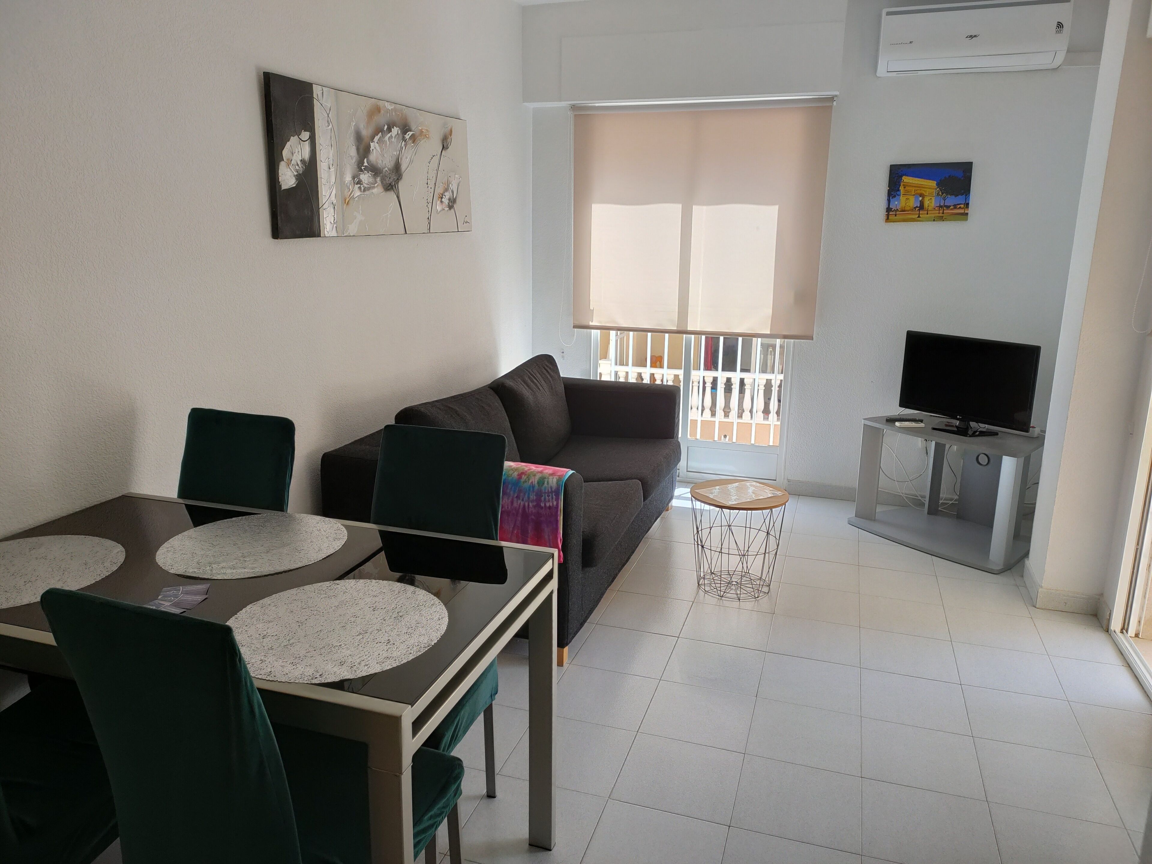 A living room with a sofa, a dining table with chairs, a TV on a stand, and artwork on the walls.