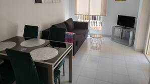 A living room with a sofa, a dining table with chairs, a TV on a stand, and artwork on the walls. - Holiday Houses - Playa del Cura 2 (Torrevieja)