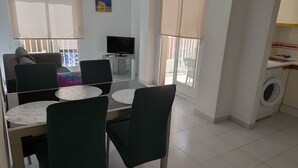 A dining area with a table and chairs, a television, and a washing machine in the background. - Holiday Houses - Playa del Cura 2 (Torrevieja)