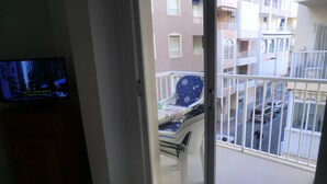 A balcony with a chair, a television, and a view of a multi-story building. - Holiday Houses - Playa del Cura 2 (Torrevieja)