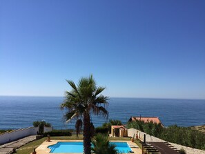 A pool with a clear view of the sea, surrounded by a white wall and a palm tree. - Sunset hause villa. private pool (Ericeira)