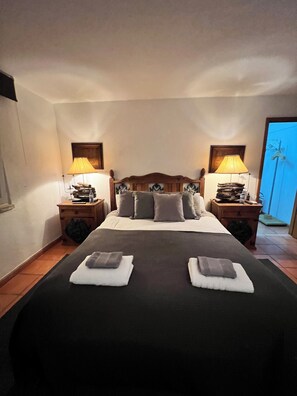 A neatly made bed with pillows and a blanket, two bedside tables with lamps, and a view of the outside. - Sunset hause villa. private pool (Ericeira)