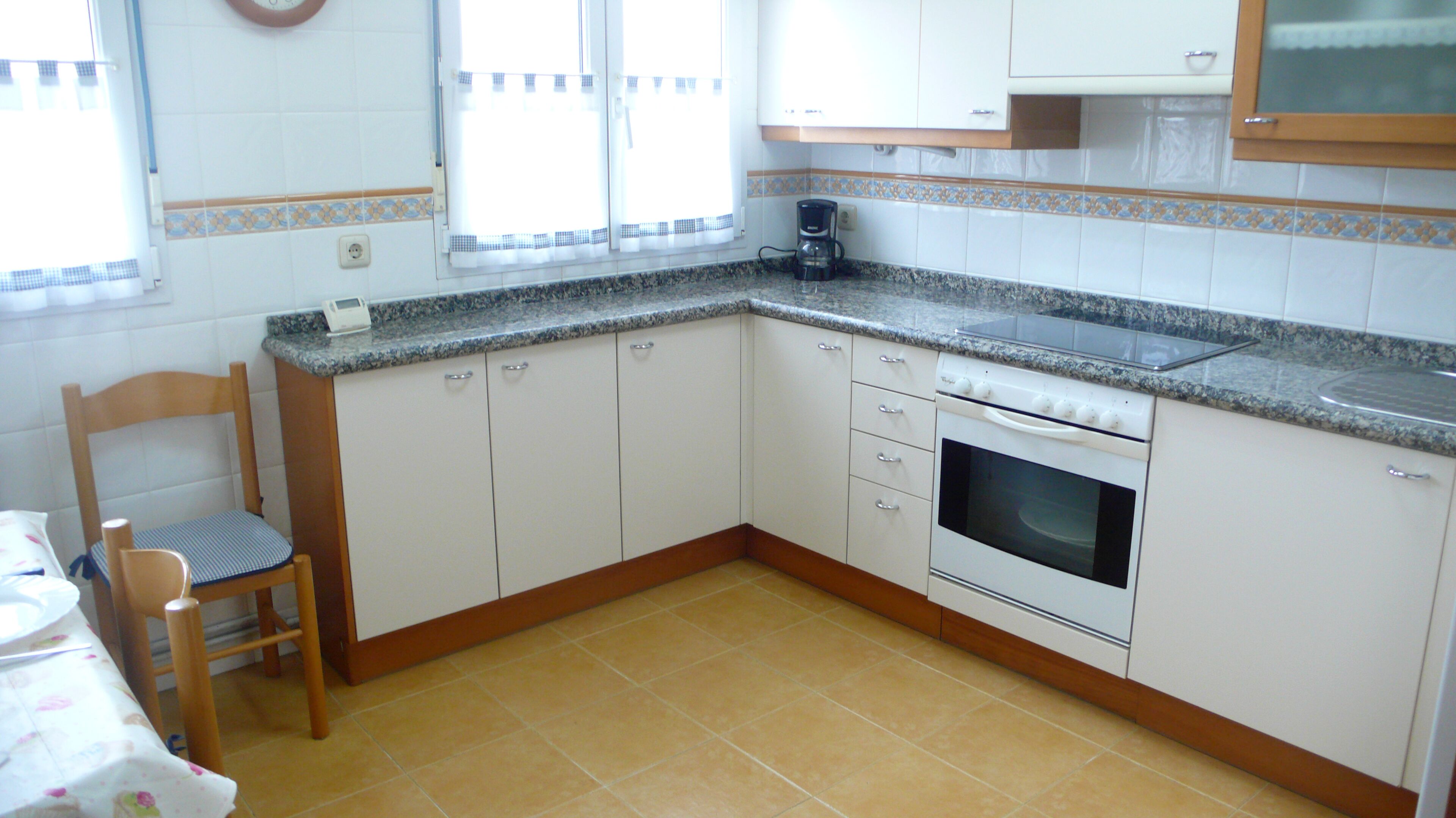 A kitchen with white cabinets, a granite countertop, a coffee maker, and a wooden chair.