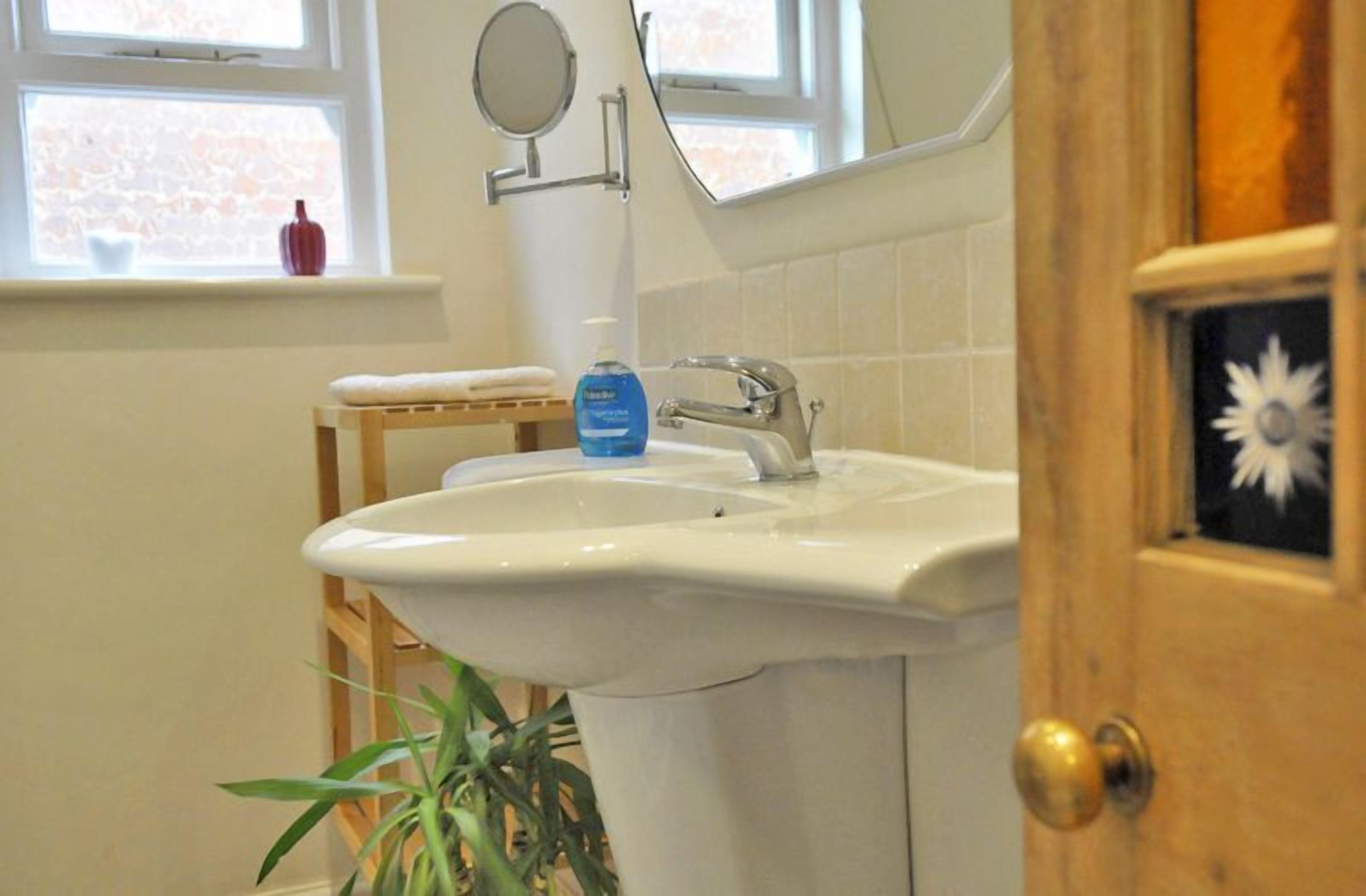 A bathroom with a white sink, a mirror, and a window with a view of a brick wall.