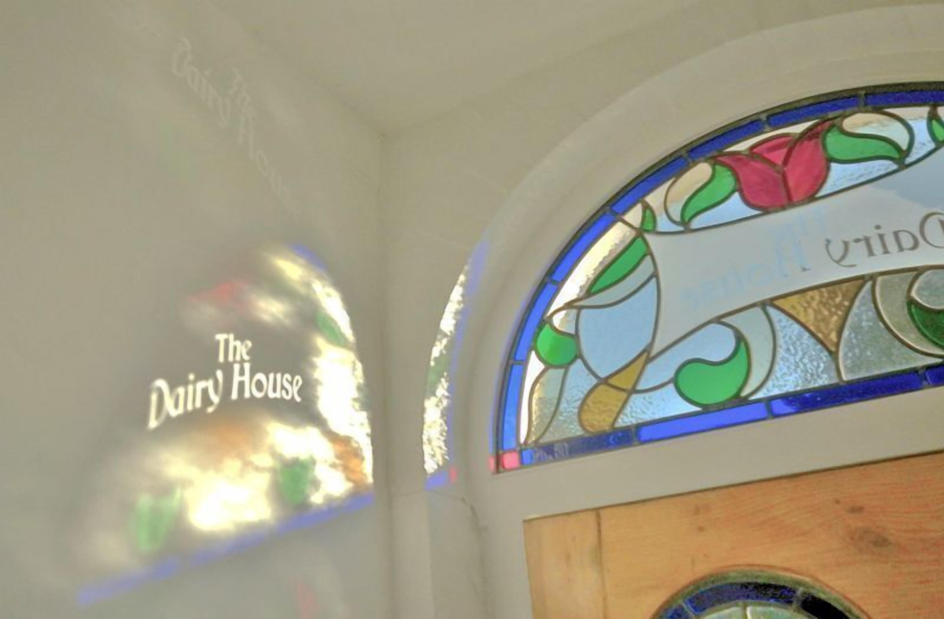 Ein Buntglasfenster mit floralem Dekor und dem Schriftzug "The Dairy House" an der Wand.