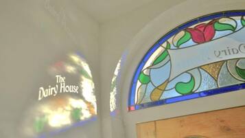 Ein Buntglasfenster mit floralem Dekor und dem Schriftzug "The Dairy House" an der Wand.
