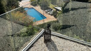 A glass-enclosed balcony with a pool, surrounded by trees and a view of the sea.
