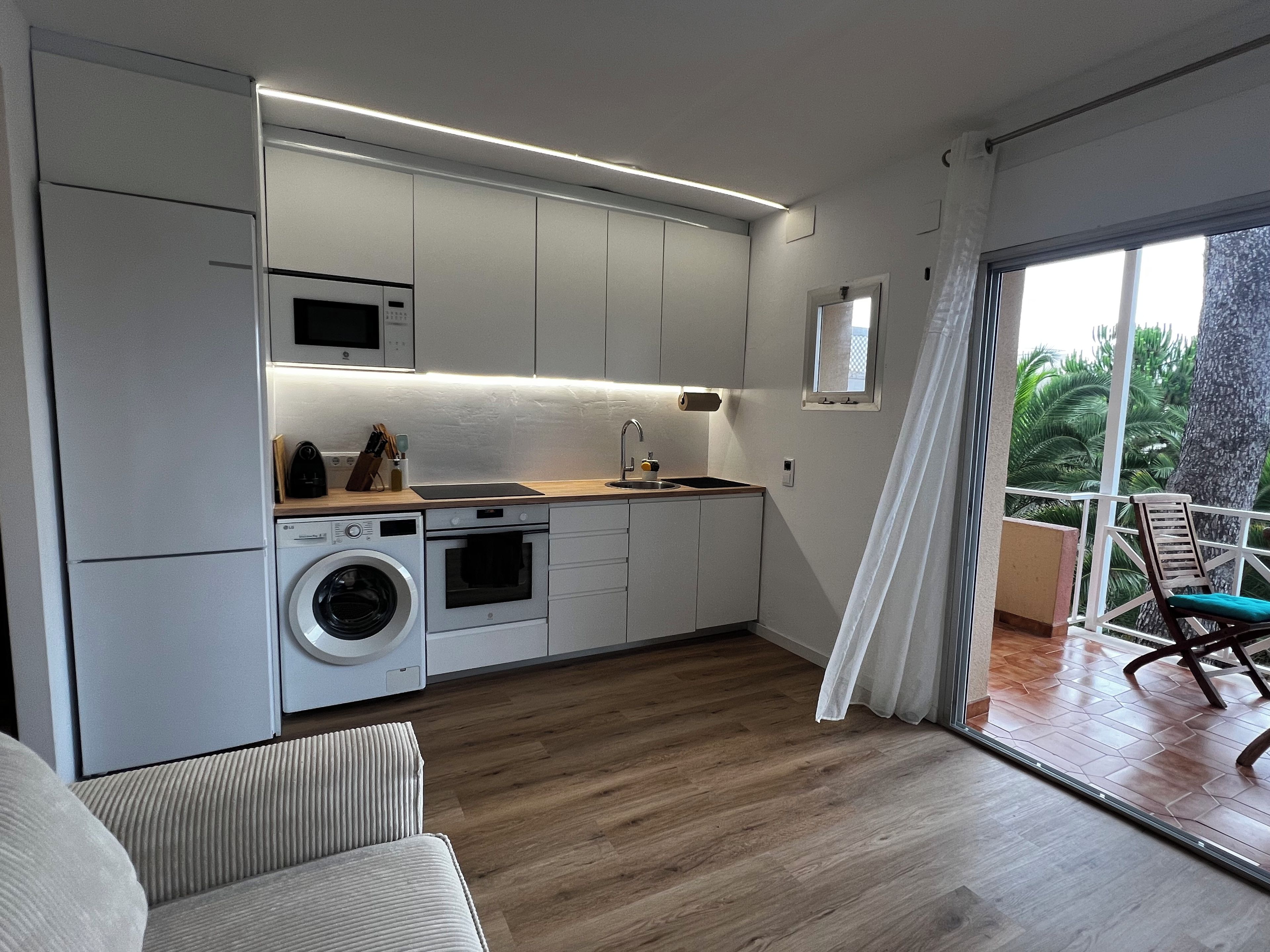 A modern kitchen with built-in appliances, a wooden countertop, and a view of the outdoors through a sliding glass door.