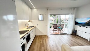 Une cuisine moderne équipée d’un lave-linge intégré, un coin repas avec une table et des chaises, et un téléviseur posé sur un meuble.