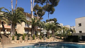 Une piscine à l’eau d’un bleu cristallin, entourée de palmiers et bordée d’un bâtiment doté de balcons.