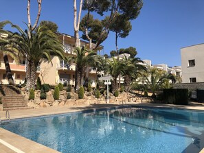 A swimming pool with clear blue water, surrounded by palm trees and a building with balconies.