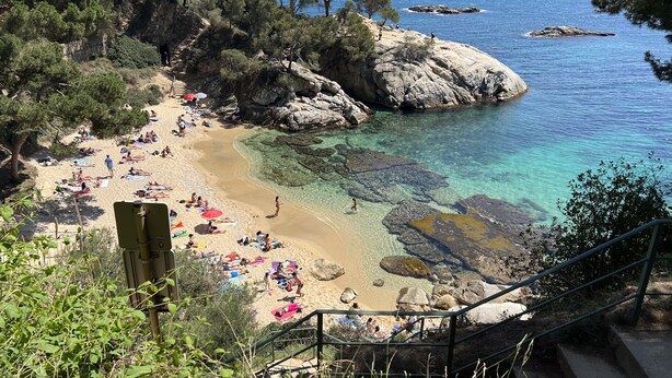 Une plage côtière aux eaux cristallines, parsemée de rochers et où l’on peut voir des gens se prélasser au soleil.