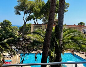 A pool area with a clear view of the sea, surrounded by trees and a building with a red roof. - Apartment/ flat - Gerona (Platja d'Aro)